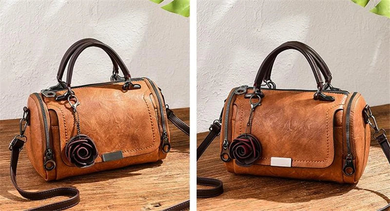 Braunes Leder-Blumen-Anhänger-Schultertasche mit dunklem Riemen auf Holzoberfläche.