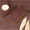 A brown genuine leather passport wallet with card holders resting on a dark brown textured fabric next to a wood slice and a 