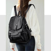 A woman is shown wearing a black vintage soft leather backpack over a white sweater and dark jeans.