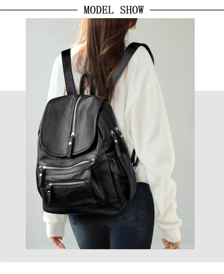 A woman is shown wearing a black vintage soft leather backpack over a white sweater and dark jeans.