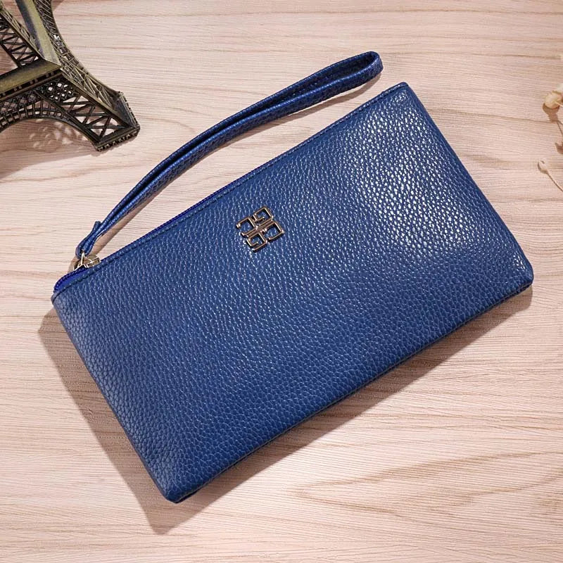 Cartera con cremallera de cuero sintético azul oscuro y logo dorado sobre una superficie de madera clara.