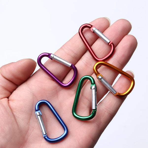 A hand holds a set of colorful aluminum carabiner hooks with silver and colored rings.