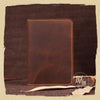 A brown genuine leather passport wallet with stitched edges resting on a dark fabric surface.