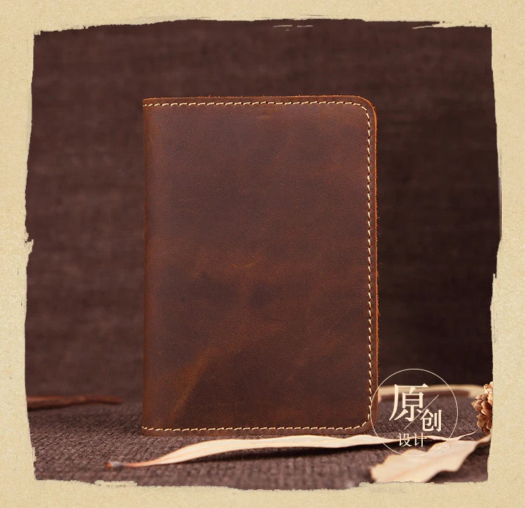 A brown genuine leather passport wallet with stitched edges resting on a dark fabric surface.