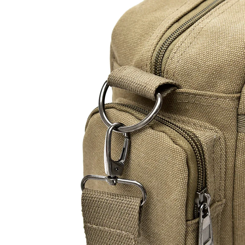 A close-up of a tan canvas crossbody messenger bag featuring brass hardware and zippered pockets.