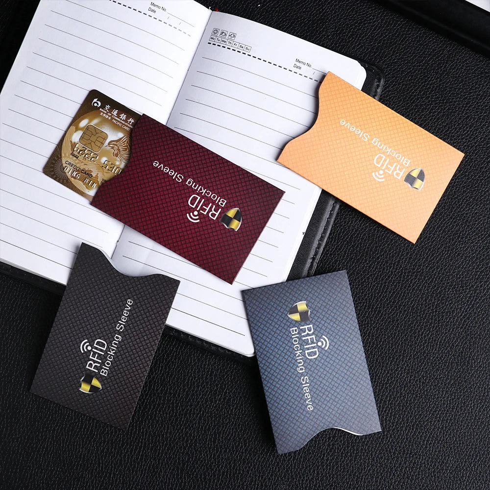 Several RFID blocking card sleeves in various colors are displayed on a black surface.