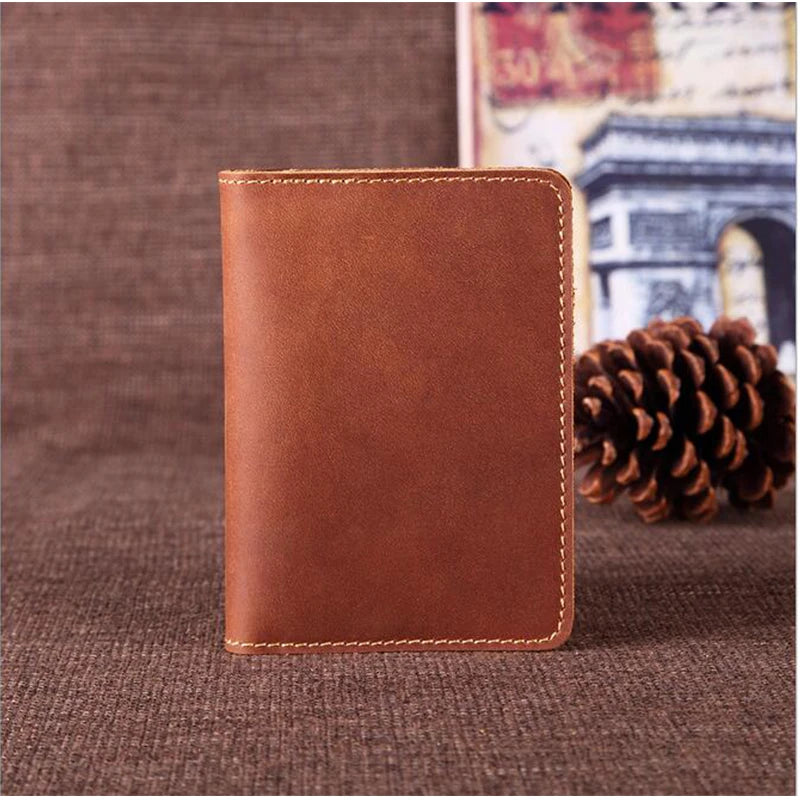 A brown genuine leather passport wallet with card holders resting on a dark brown fabric next to a pine cone.