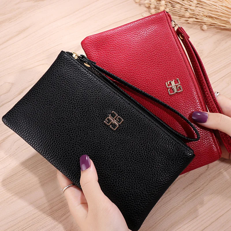 Cartera con cremallera de cuero sintético negro junto a una cartera de cuero sintético rojo sobre una superficie de madera.