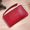 Cartera con cremallera de cuero PU roja sobre una superficie de madera clara, con correa de cuero visible.