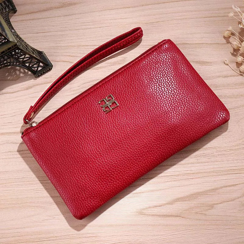 Cartera con cremallera de cuero PU roja sobre una superficie de madera clara, con correa de cuero visible.