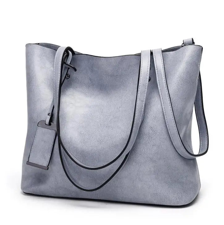 A light gray waxed leather bucket bag with dual straps shown from the front.