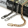 A close-up of a gold-toned metal bag chain strap with silver clips displayed on a dark surface.
