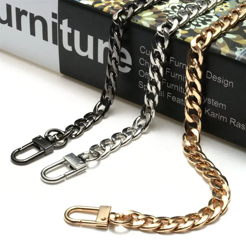 A close-up of a gold-toned metal bag chain strap with silver clips displayed on a dark surface.