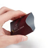 A hand holds a dark red RFID blocking card sleeve with a black pattern and an RFID symbol printed on it.