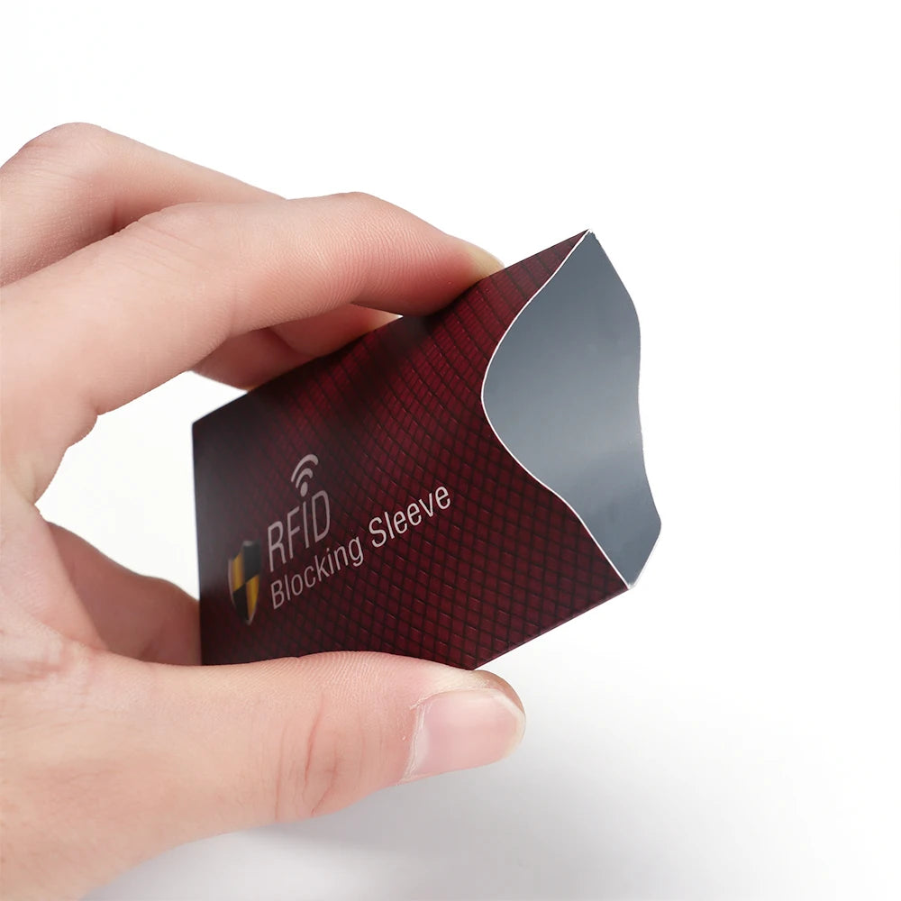 A hand holds a dark red RFID blocking card sleeve with a black pattern and an RFID symbol printed on it.