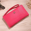 Cartera de cuero PU rosa brillante con cremallera y correa delgada, tumbada sobre una superficie de madera clara.