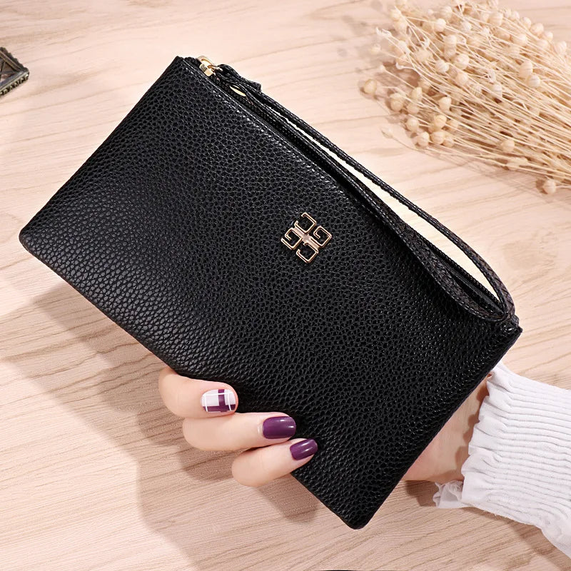 Cartera con cremallera de cuero PU negro y detalles dorados sostenida por una mano sobre una superficie de madera.