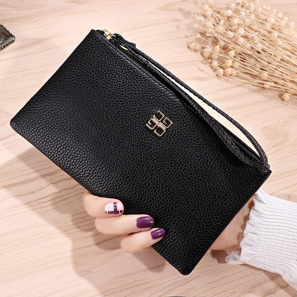 A black PU leather zipper wallet with gold detailing is held by a hand on a wooden surface.