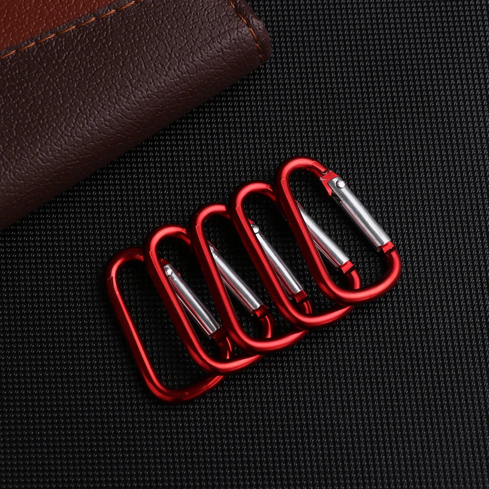 A set of five red aluminum carabiner hooks resting on a dark fabric surface.