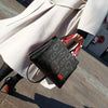 Une femme portant un manteau beige tient un sac bandoulière en cuir PU noir avec des accents rouges.