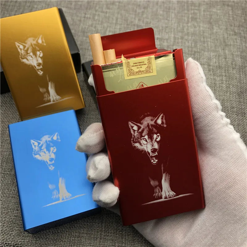 A red cigarette case with a wolf engraving is held in a hand next to a gold cigarette case.