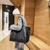 A person wearing a white beanie is holding an oversized black PU leather tote bag in a modern wooden interior.
