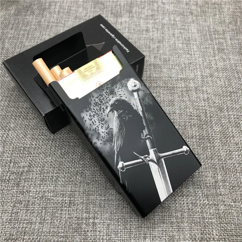 A black cigarette case with a silver sword design and a gold-colored cigarette inside, resting on a gray fabric surface.