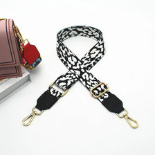 A black and white patterned adjustable strap for a messenger bag with gold hardware.