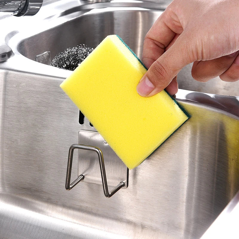 Une main pose une éponge jaune sur un organisateur de grille à éponge en acier inoxydable.