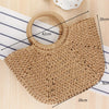 A handwoven straw moon bag with a round top handle shown on a wooden surface.