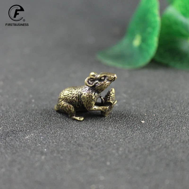 A vintage brass rat figurine is shown resting on a dark surface.