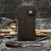 A dark brown genuine leather bifold wallet with a leather strap and metal chain resting on a dark fabric.