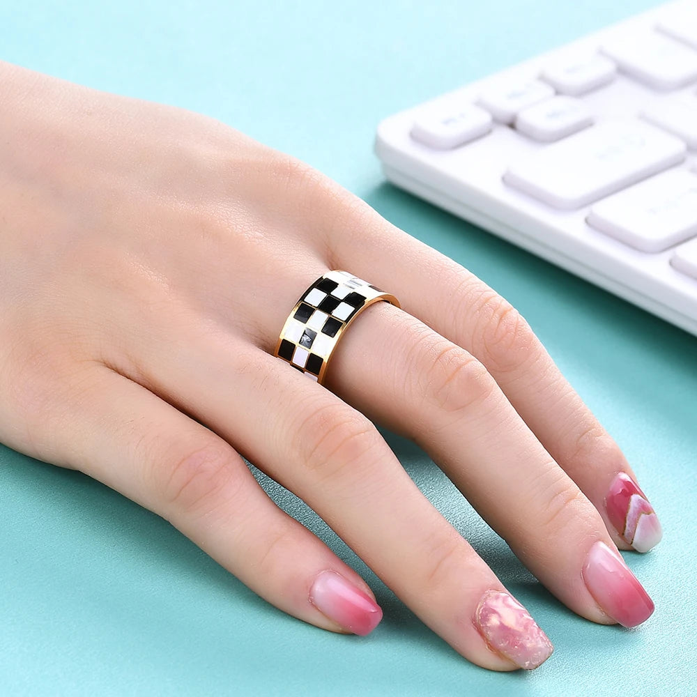 Gold-toned checkerboard dome rings worn on a hand next to a white computer keyboard.