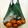 A green mesh grocery tote bag filled with fresh oranges and other produce.