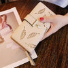 Una mano sostiene un bolso clutch de cuero PU beige con patrones de hojas grabadas en oro sobre una mesa de madera oscura.