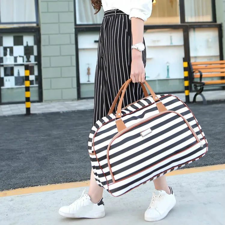 A woman wearing a white top and black striped skirt holds a black and white leather travel duffel bag outdoors.