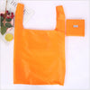An orange eco-friendly foldable shopping bag next to a small orange bag tag.