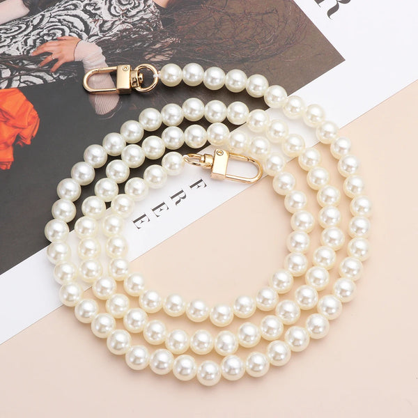 A strand of white pearls with gold clasps laid out on a light background.