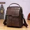 A dark brown vintage PU leather crossbody messenger bag resting on a wooden surface next to a grandfather clock.