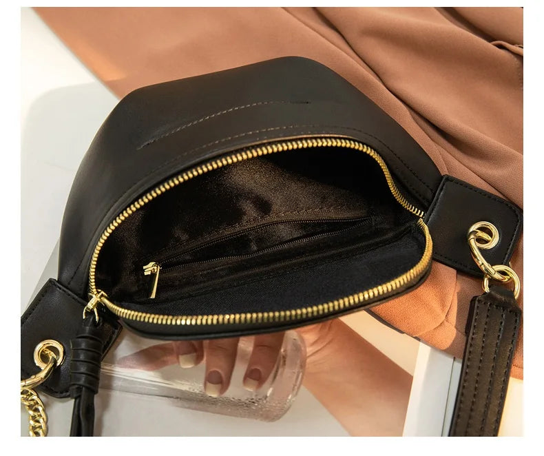 A black PU leather crossbody sling bag with gold hardware is shown against a tan fabric background.