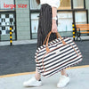 A woman is standing outdoors holding a large striped black and white PU leather travel duffel bag.