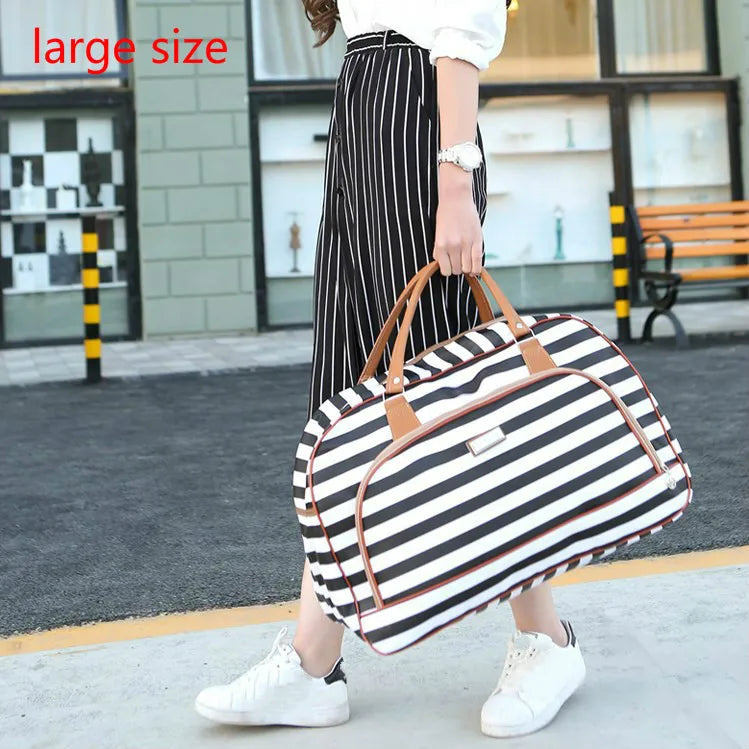 A woman is standing outdoors holding a large striped black and white PU leather travel duffel bag.