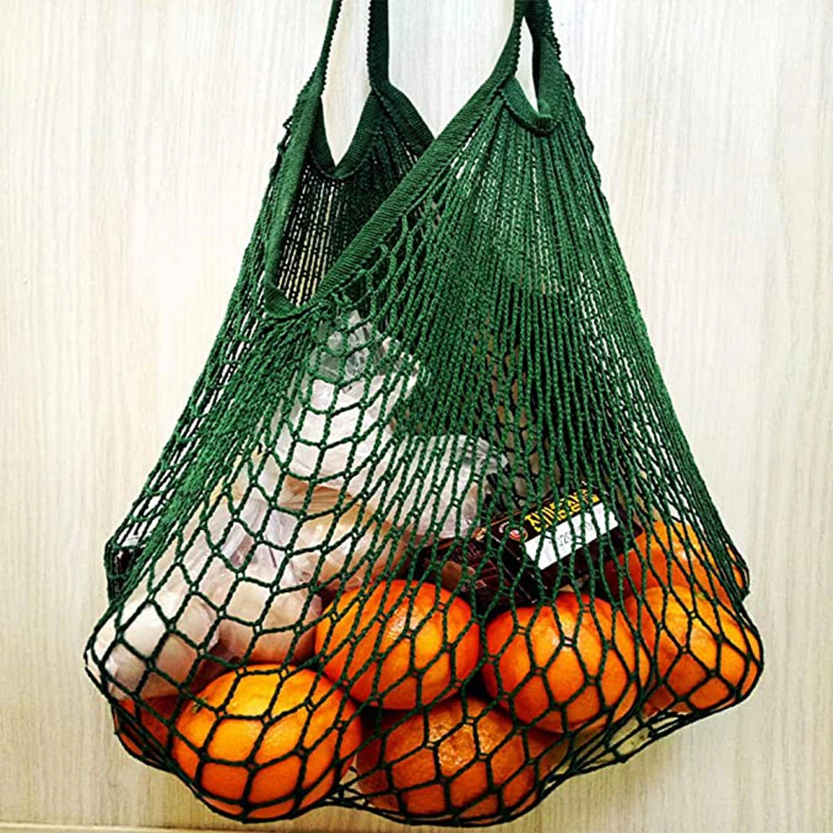 A green mesh grocery tote bag filled with fresh oranges and other produce.