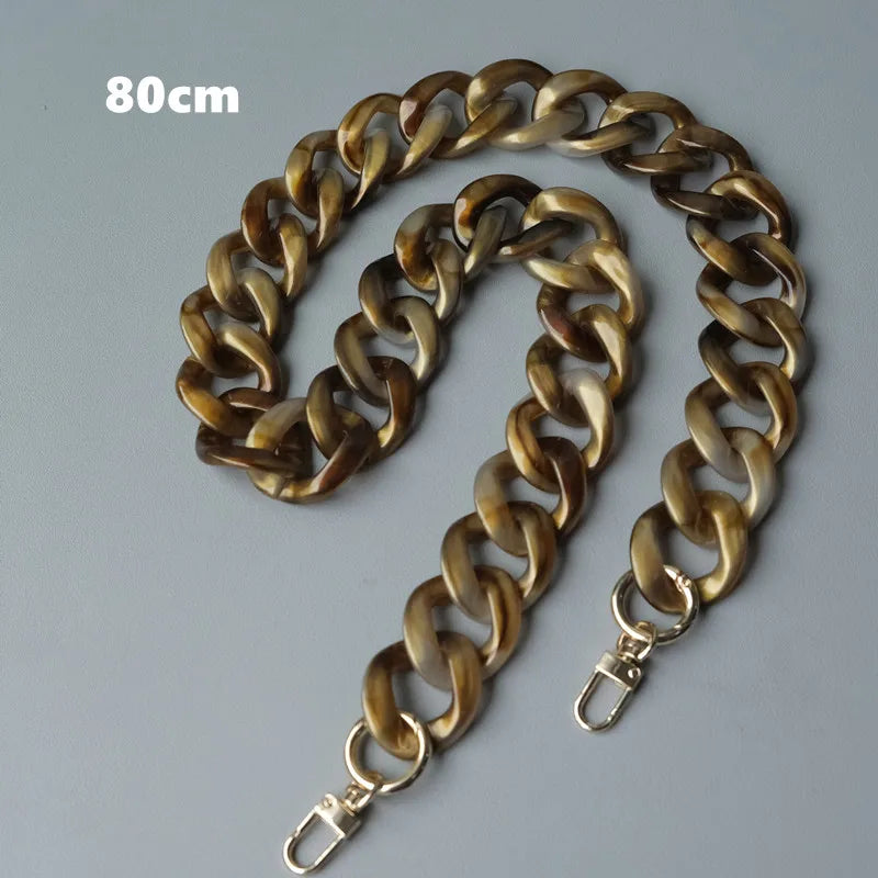 Bolso de cadena de hombro de resina dorada, mide 80 cm, mostrado enrollado sobre fondo gris.