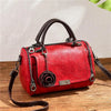 Rote Lederhandtasche mit Blumenanhänger und braunem Riemen auf Holzoberfläche.