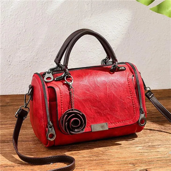 Rote Lederhandtasche mit Blumenanhänger und braunem Riemen auf Holzoberfläche.