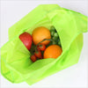 A bright lime green foldable shopping bag contains an orange, a red apple, and a bunch of green grapes.