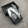 A black cigarette case with a silhouette of a bird against a moon background is displayed on a gray fabric surface.