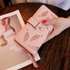 Una mano sostiene un bolso clutch de cuero PU rosa con patrones de hojas grabados sobre una mesa de madera oscura.