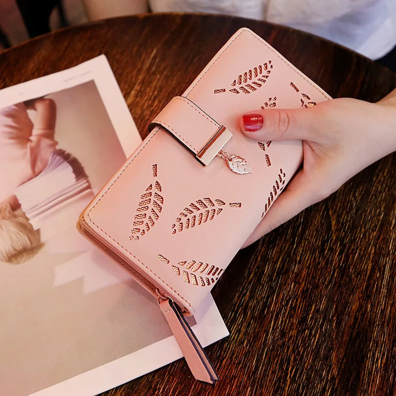 Una mano sostiene un bolso clutch de cuero PU rosa con patrones de hojas grabados sobre una mesa de madera oscura.